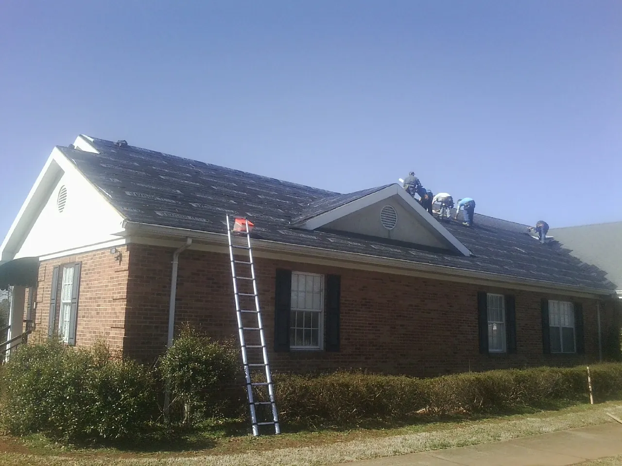Crew tearing shingles off a brick ranch roof with a ladder set — Metal Roof Repair work by our crew in Scotland