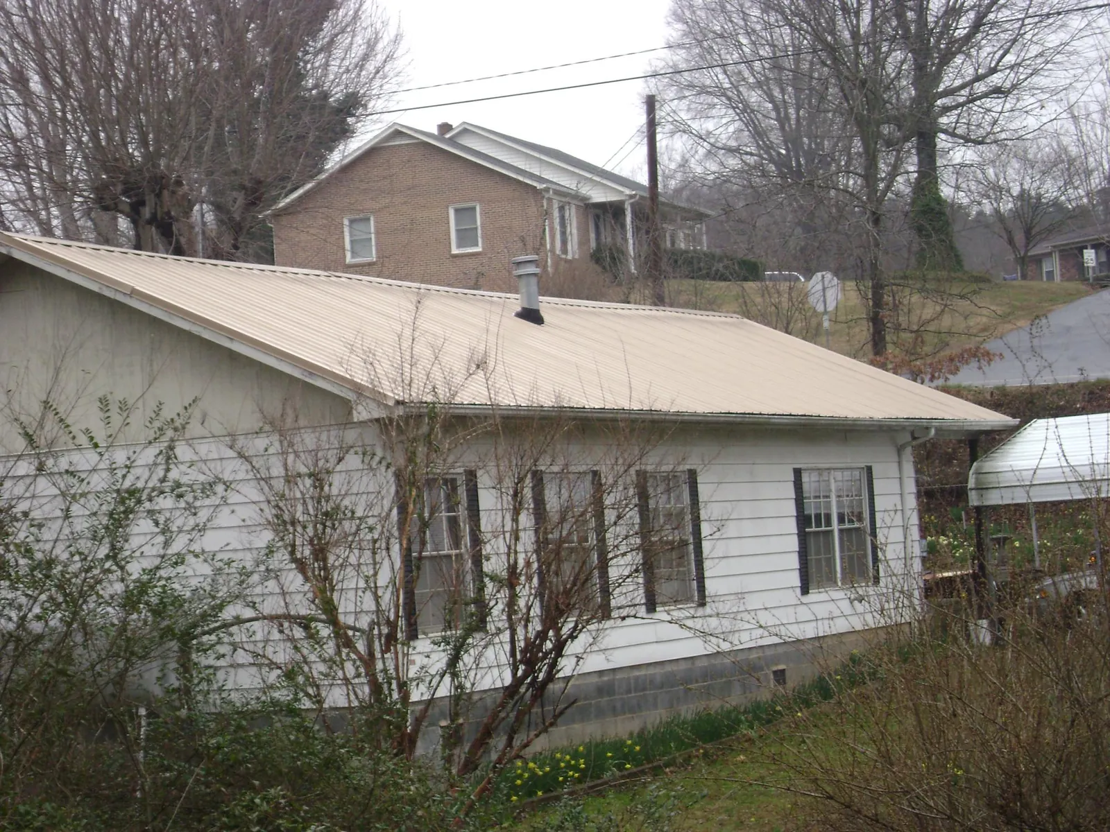 Tan metal roof on a white sided house set into a hillside — Commercial Roofing by Roofing Brothers in Scotland